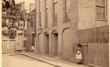 a sepia-toned photograph of a tall building and two women standing on the sidewalk outside of it